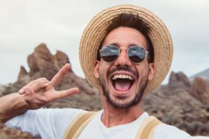 A man in sunglasses and a hat holds up a peace sign as he tells his friends about Lovett Dental in Webster, TX