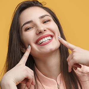 A woman points to her smile after getting cosmetic dentistry in Webster, TX