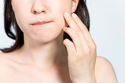 young woman who checks her skin. acne treatment. woman with swollen cheeks in need of TMJ Treatment